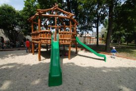 Prírodné drevené detské ihrisko v mestskom parku, ručne opracované guľatinové konštrukcie, lezecké steny, lanové prechody, zelená šmýkačka, štrkový povrch , pre deti